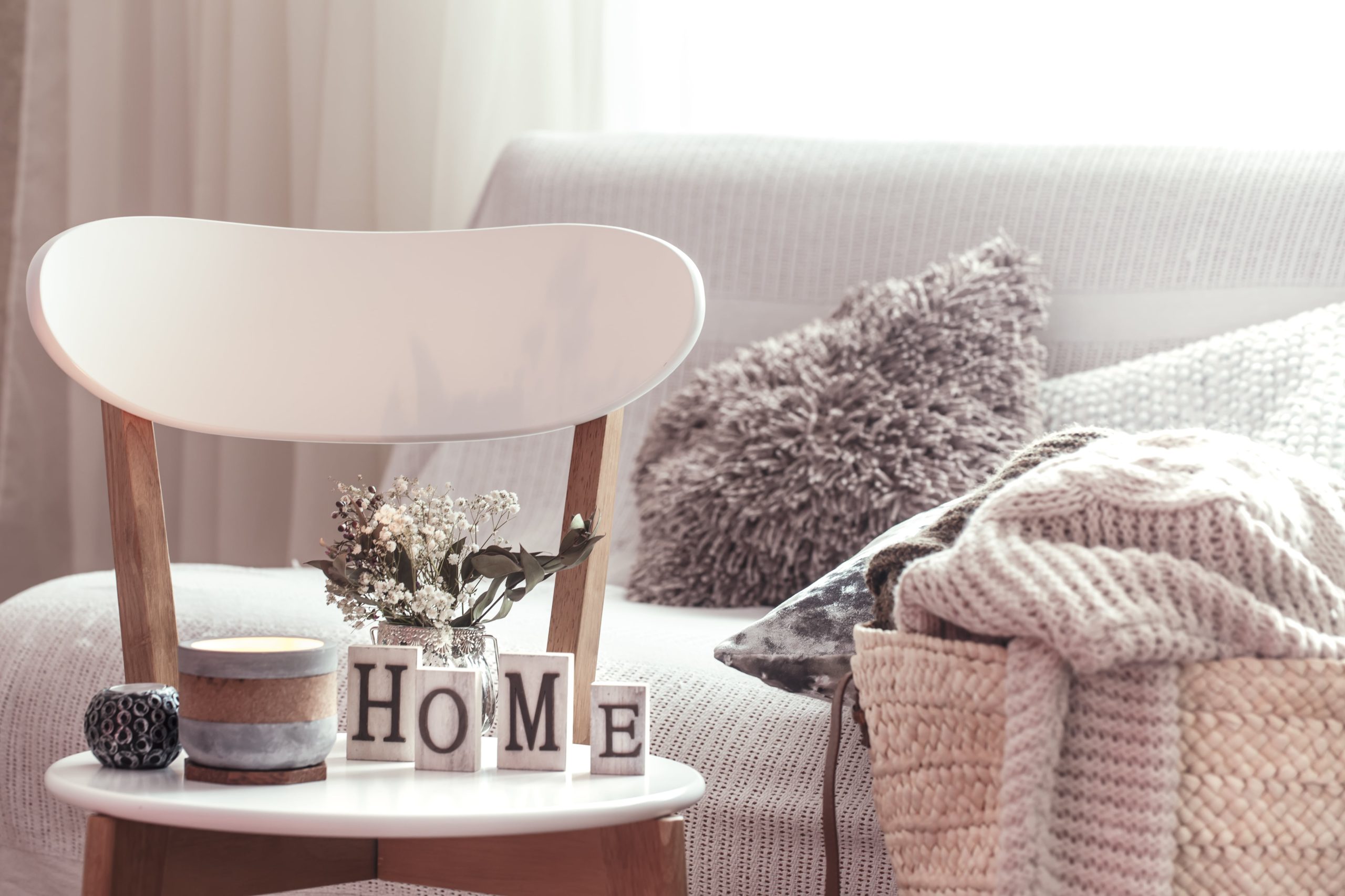 chic-interior-house-candles-vase-with-flowers-with-wooden-letters-home-wooden-white-chair-sofa-wicker-basket-with-cushions-background-home-decoration-min